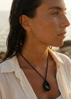 Woman wearing a black cord necklace and standing on a rocky coastline with ocean view