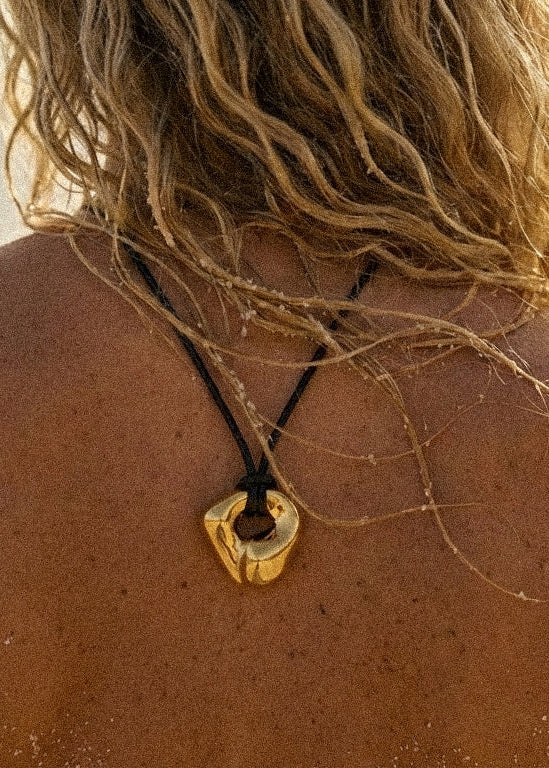 Person on a beach with a necklace featuring a gold pendant